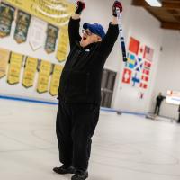 Curling athlete celebrates with both arms in the air