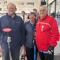 Three Special Olympics curling athletes smile at the side of the rink