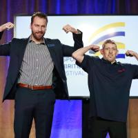 Canucks player Tucker Poolman and SOBC athlete Mike Palitti flexing their arms on stage