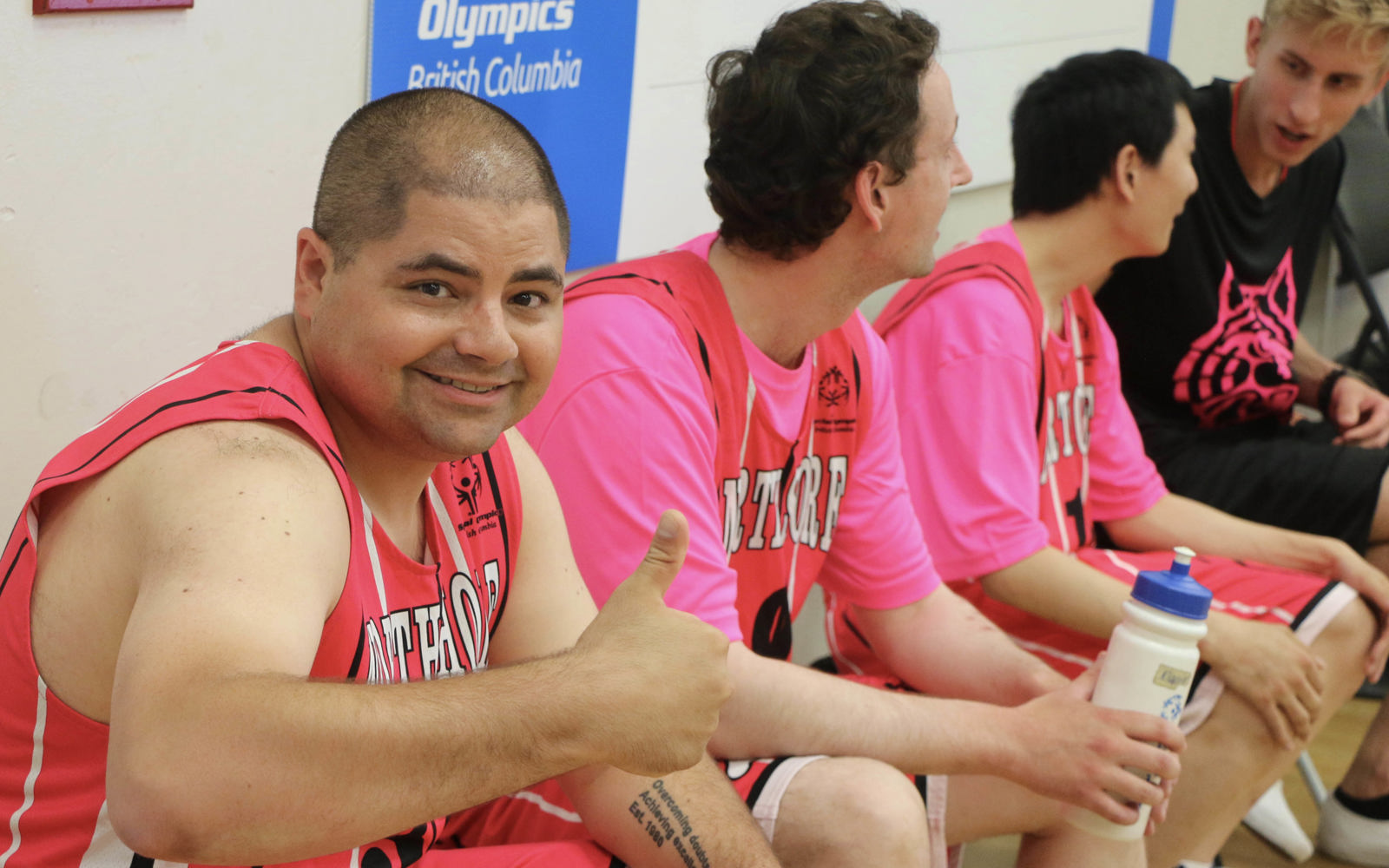 Special Olympics BC basketball athlete on the player's bench looks to the camera, smiles and gives a thumbs up.