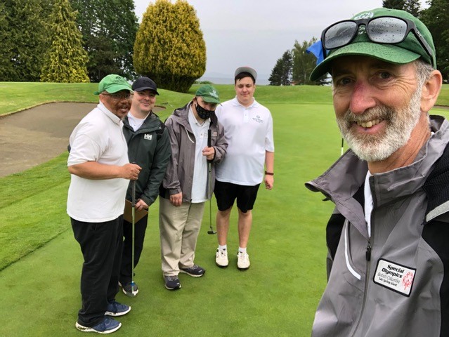 A group of four golfers are on the green posing for a photo with their coach. A group of four golfers are on the green posing for a photo with their coach.