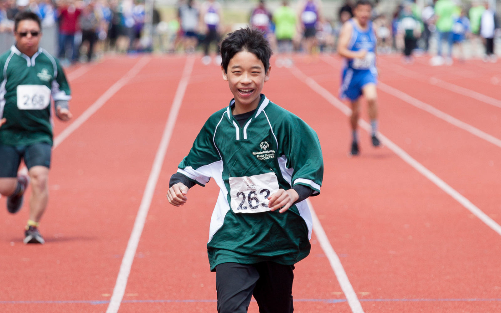 A young Special Olympics BC athlete runs towards the finish line in a 100 m sprint.