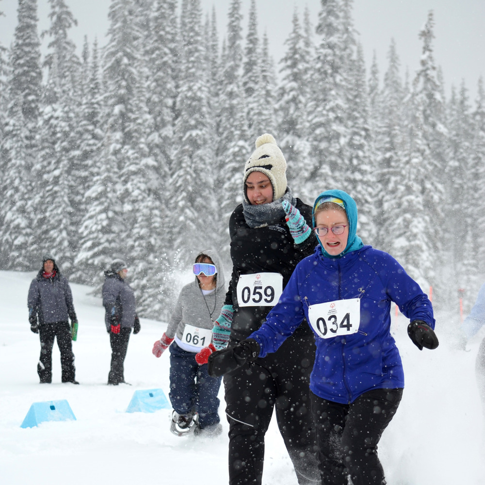 A pair of athletes with intellectual disabilities charge through the snow in their snowshoe race during the 2019 Special Olympics BC Provincial Winter Games.