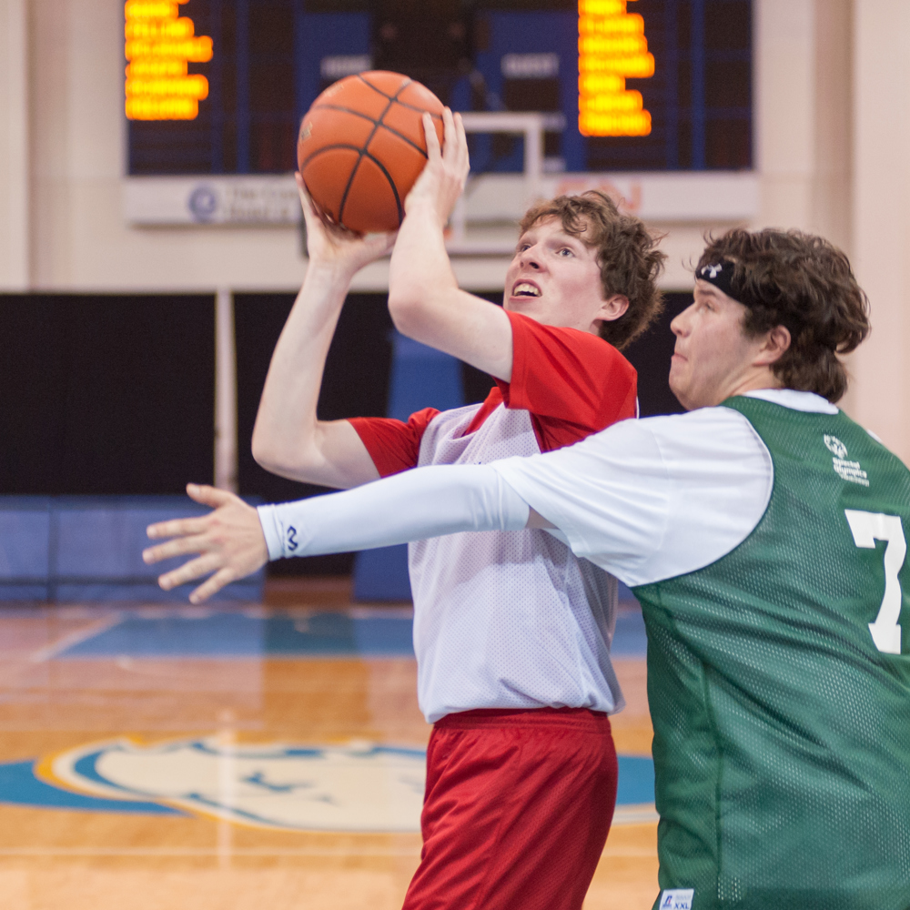 One Special Olympics BC basketball athlete plays defense against another athlete attempting to shoot the ball.