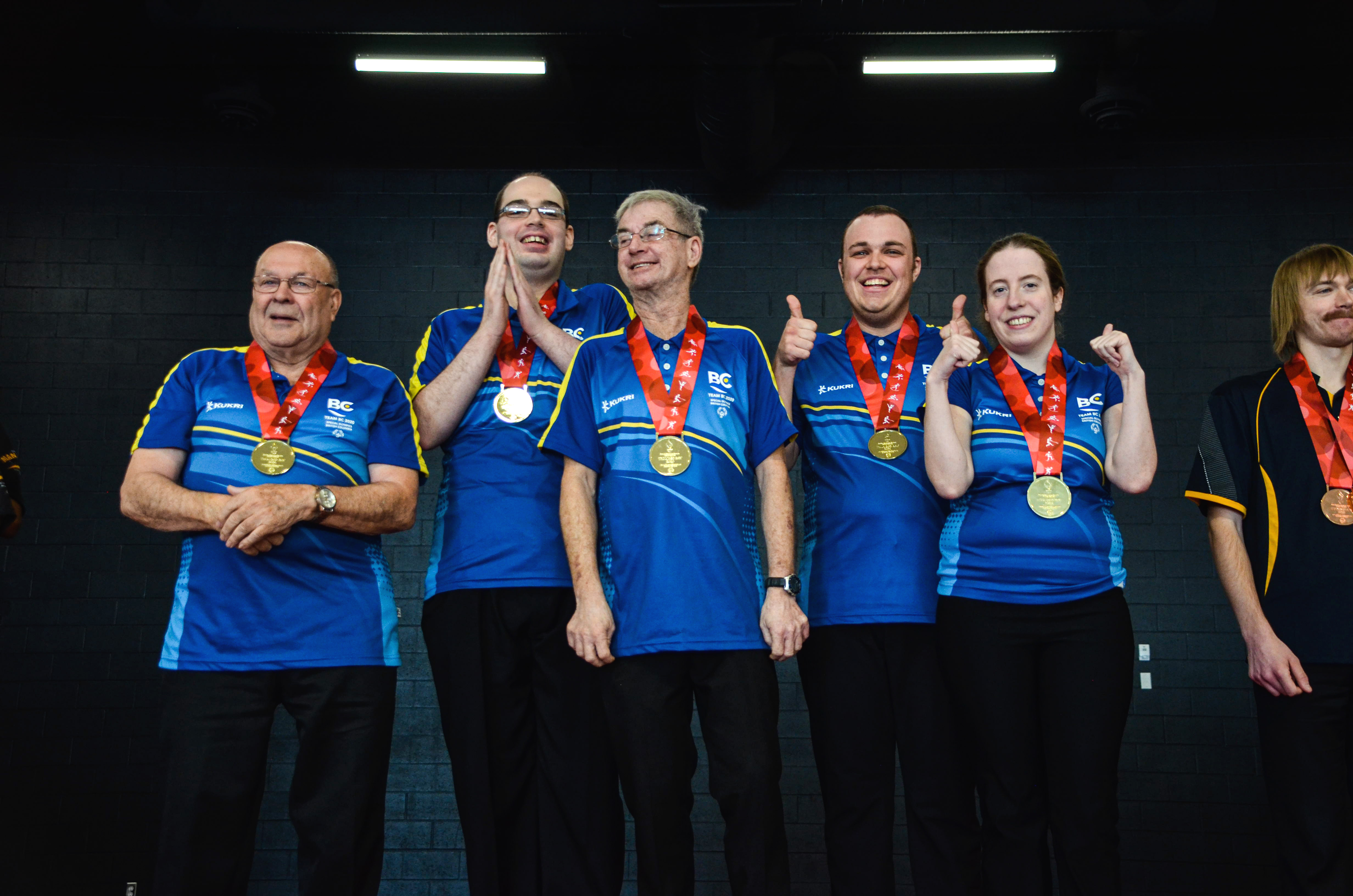 Five athletes with intellectual disabilities proudly stand together with their gold medals hung around their necks. 