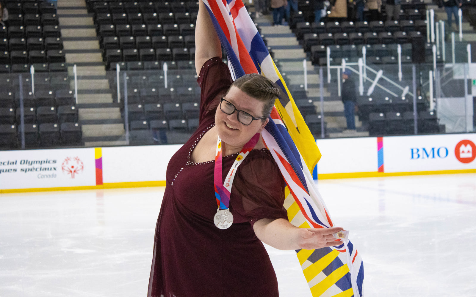Special Olympics BC athlete poses with the provincial flag after receiving a silver medal at the 2024 Special Olympics Canada National Winter Games.
