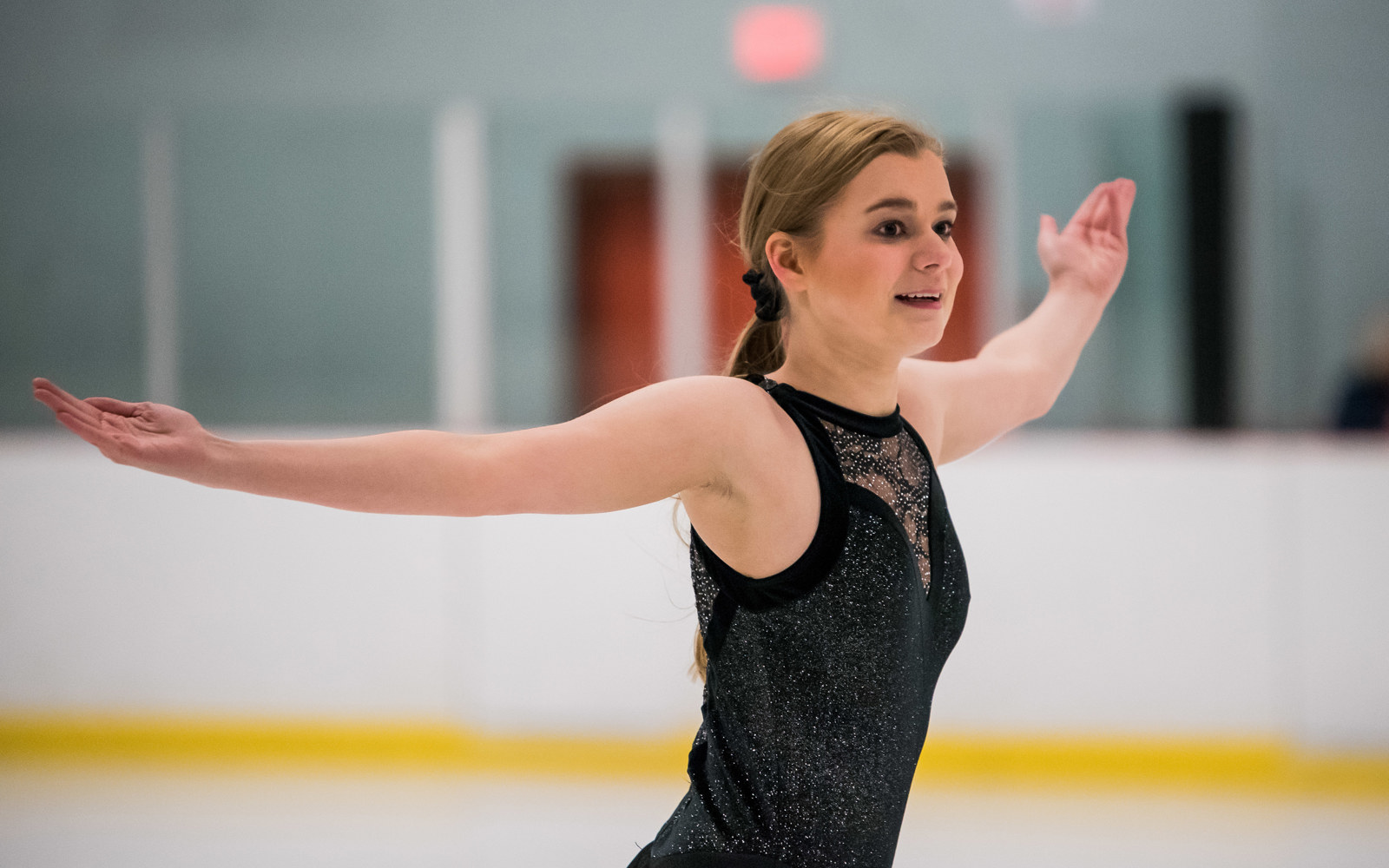 Special Oylmpics BC figure skating athlete finishes her performance with her arms outstretched and a satisfied smile on her face.