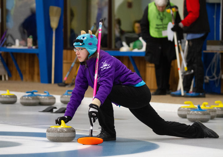 Special Olympics BC curling athlete positions herself with her broom and rock to prepares for her throw down the rink.