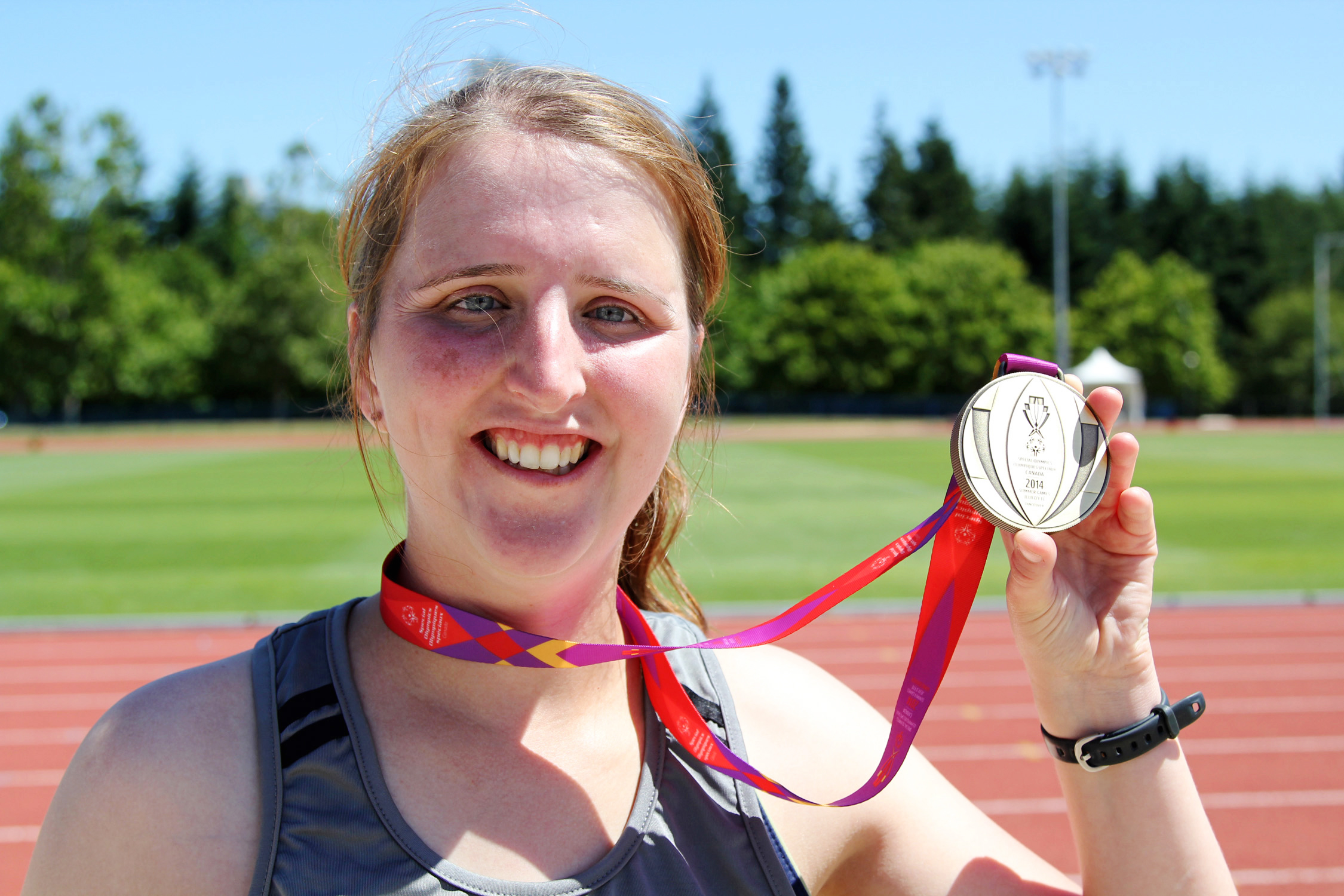 Special Olympics BC athlete Amanda proudly holds up her silver medal after competing in track and field.