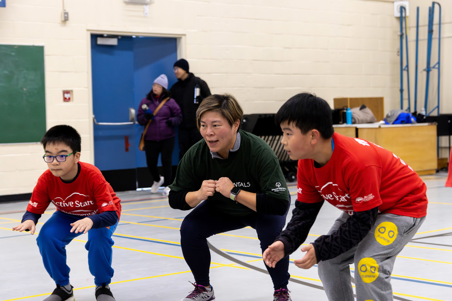 Two young boys with intellectual disabilities join their coach in warm-up exercises.