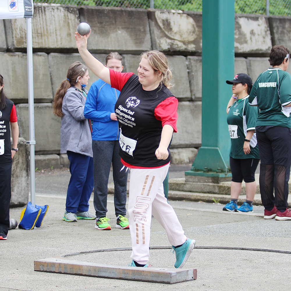 Special Olympics BC athlete throws shot put with other competitors looking on during track and field competition.