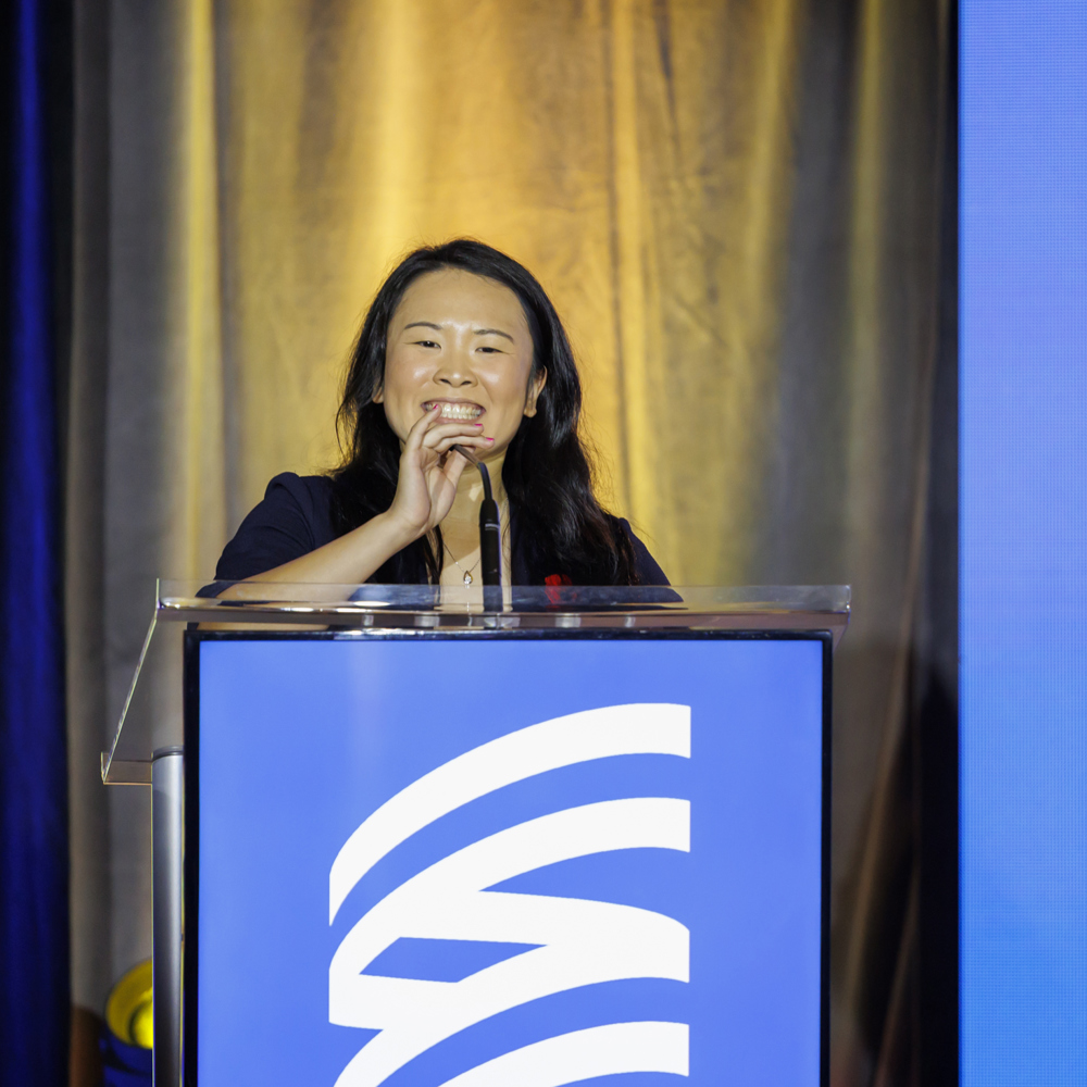 Special Olympics BC athlete Susan Wang speaks from a podium as co-emcee at the 2024 Sports Celebrities Festival.