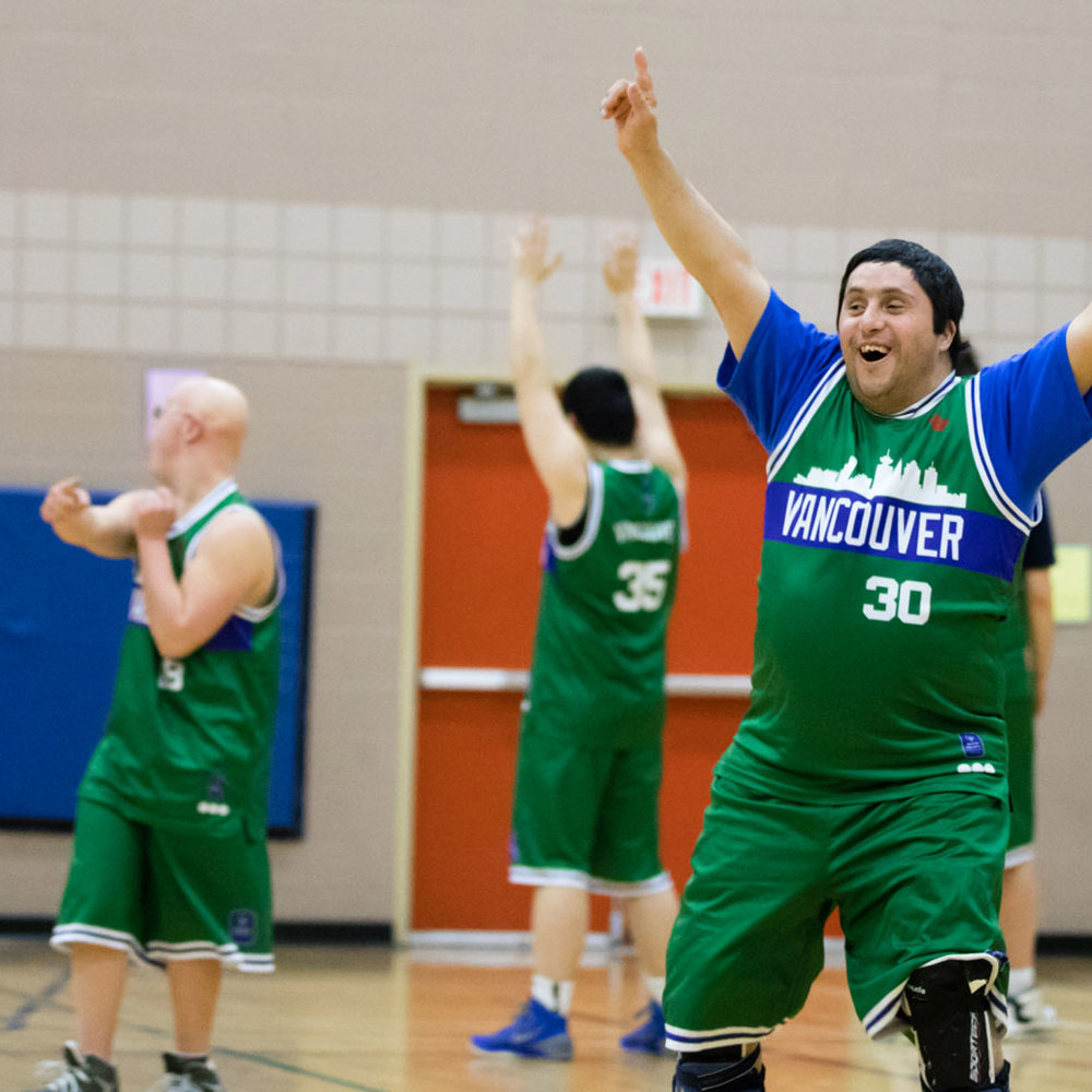 Special Olympics BC basketball athlete raises his hands in their air after winning the game.