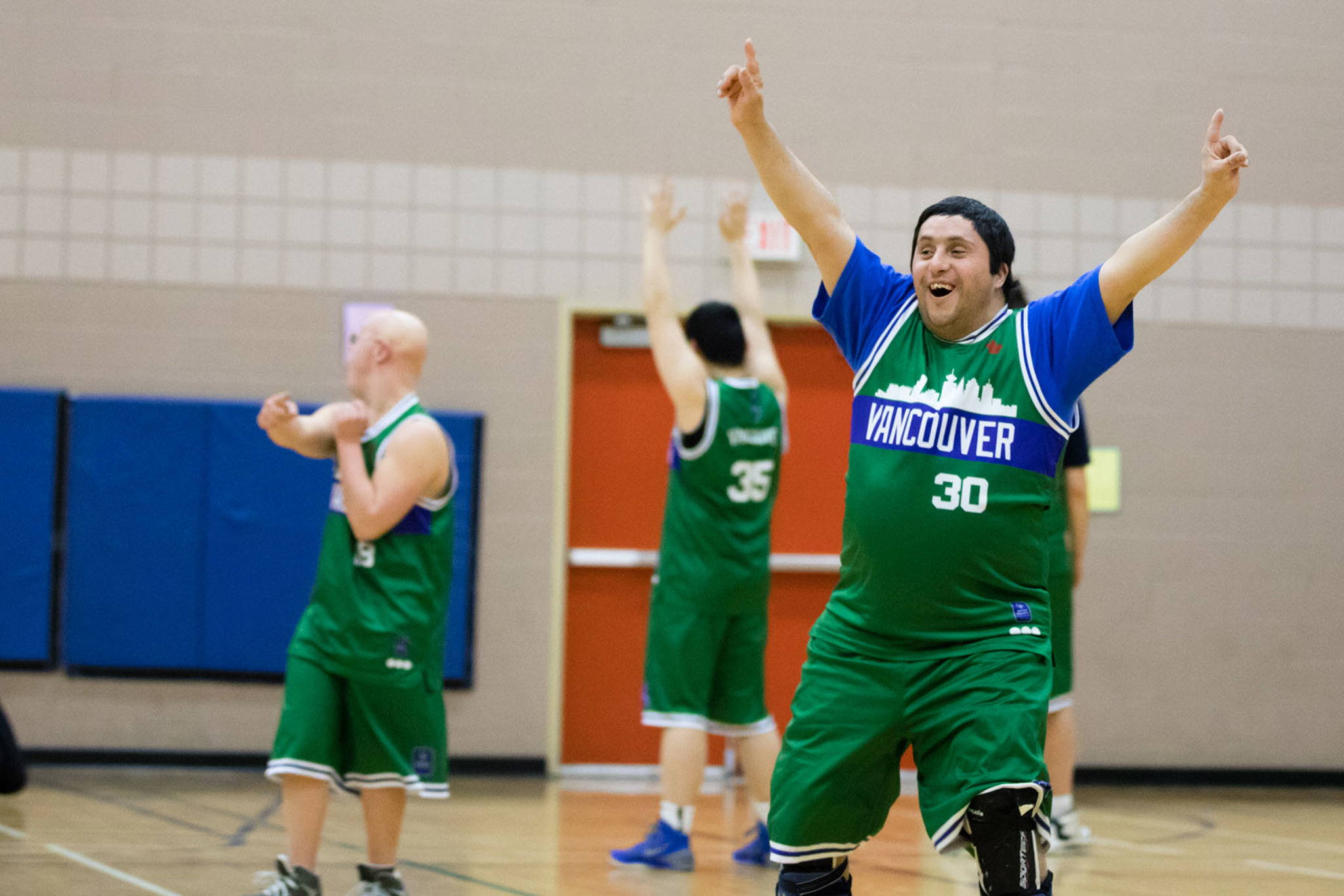 Special Olympics BC basketball athlete raises his hands in their air after winning the game.