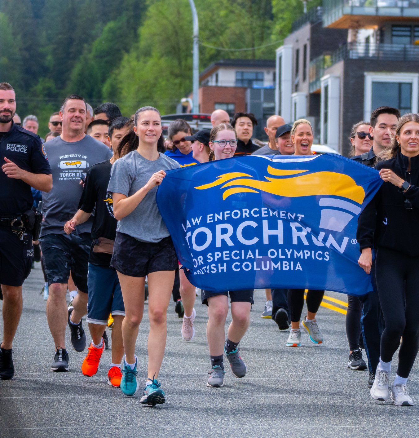 A group of participants run together holding a banner at the Port Moody Police Department Law Enforcement Torch Run Torch Run event. A group of participants run together holding a banner at the Port Moody Police Department Law Enforcement Torch Run Torch Run event.