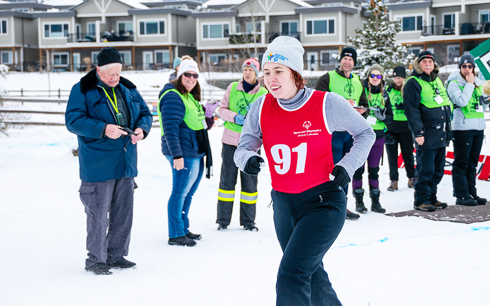 An athlete with intellectual disabilities wearing a red race bib participates in a snowshoeing race while volunteers and coaches watch.