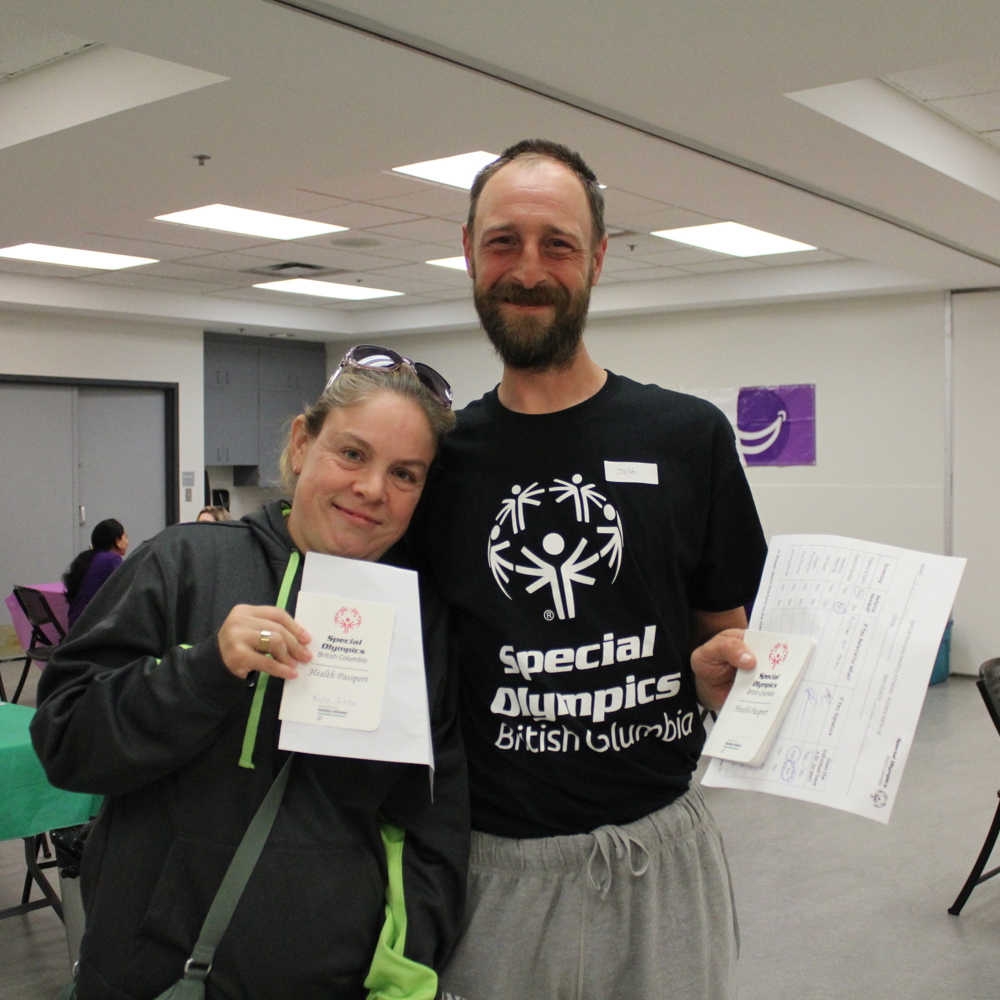 Two athletes hold their health passports and smile at the camera.