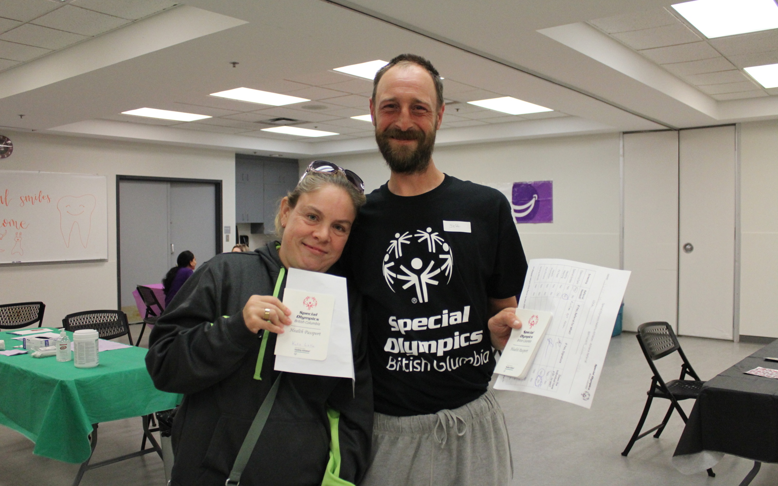 Two athletes hold their health passports and smile at the camera.