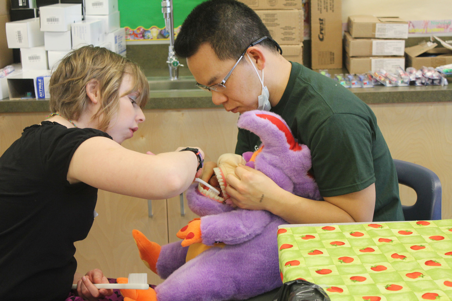 At a Special Smiles event, a volunteer holds a stuffed animal's mouth open so a young girl can practice brushing them. 