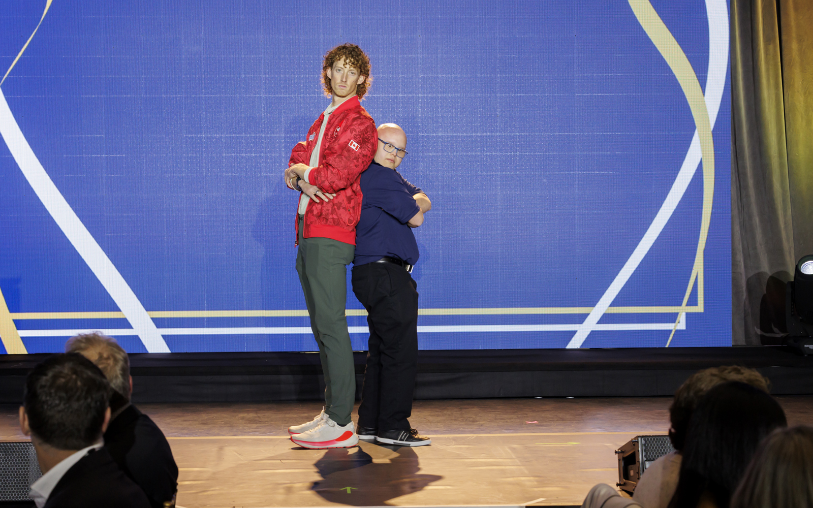 Sport Celebrtity Evan Dunfee poses with his arms crossed back-to-back with Special Olympics BC athlete on stage.