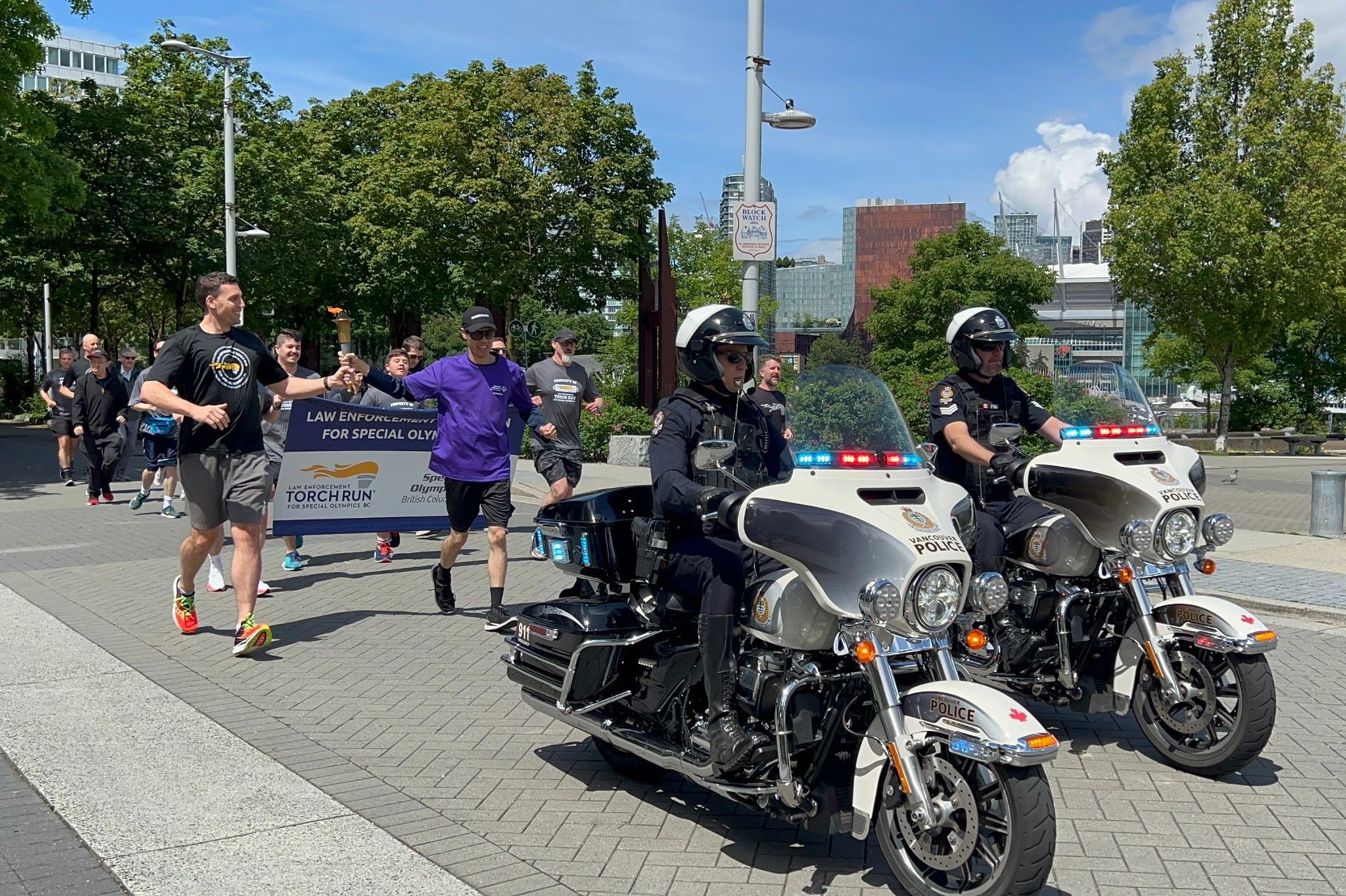 Participants run behind a police escort by two motorcycle officers while carrying the Law Enforcement Torch Run flame.