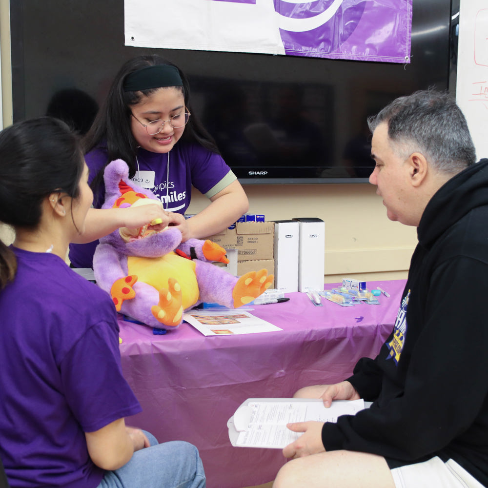 An athlete demonstrates she knowns how to brush teeth to two spectators sitting in front of her. 