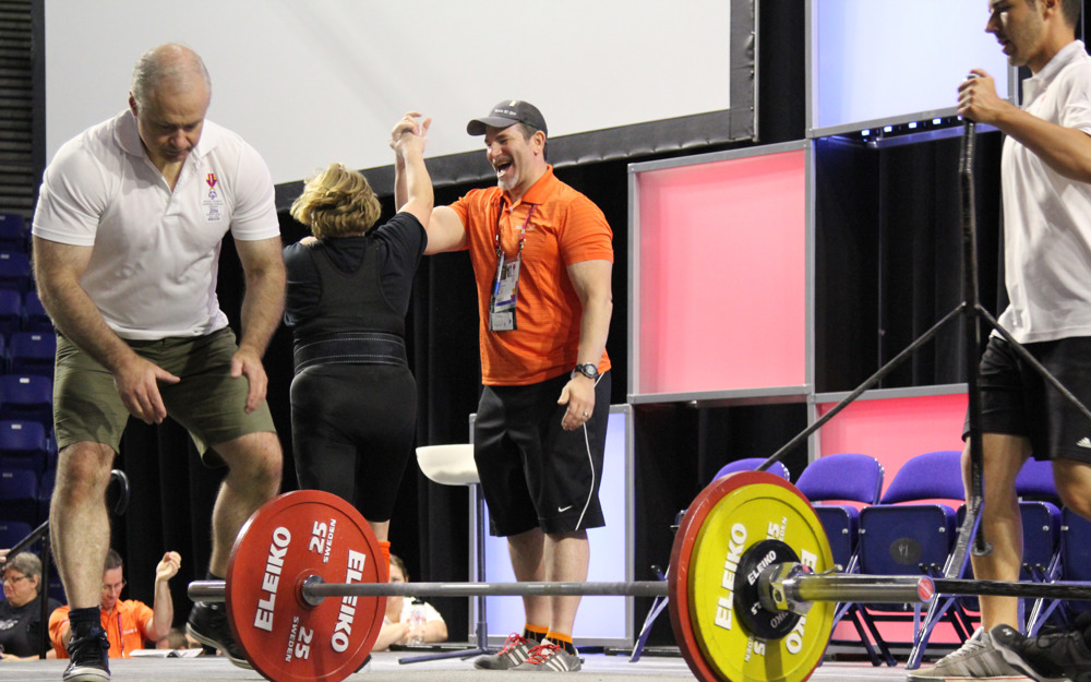 A powerlifting athlete and her coach high five each other after a good lift at a competition.