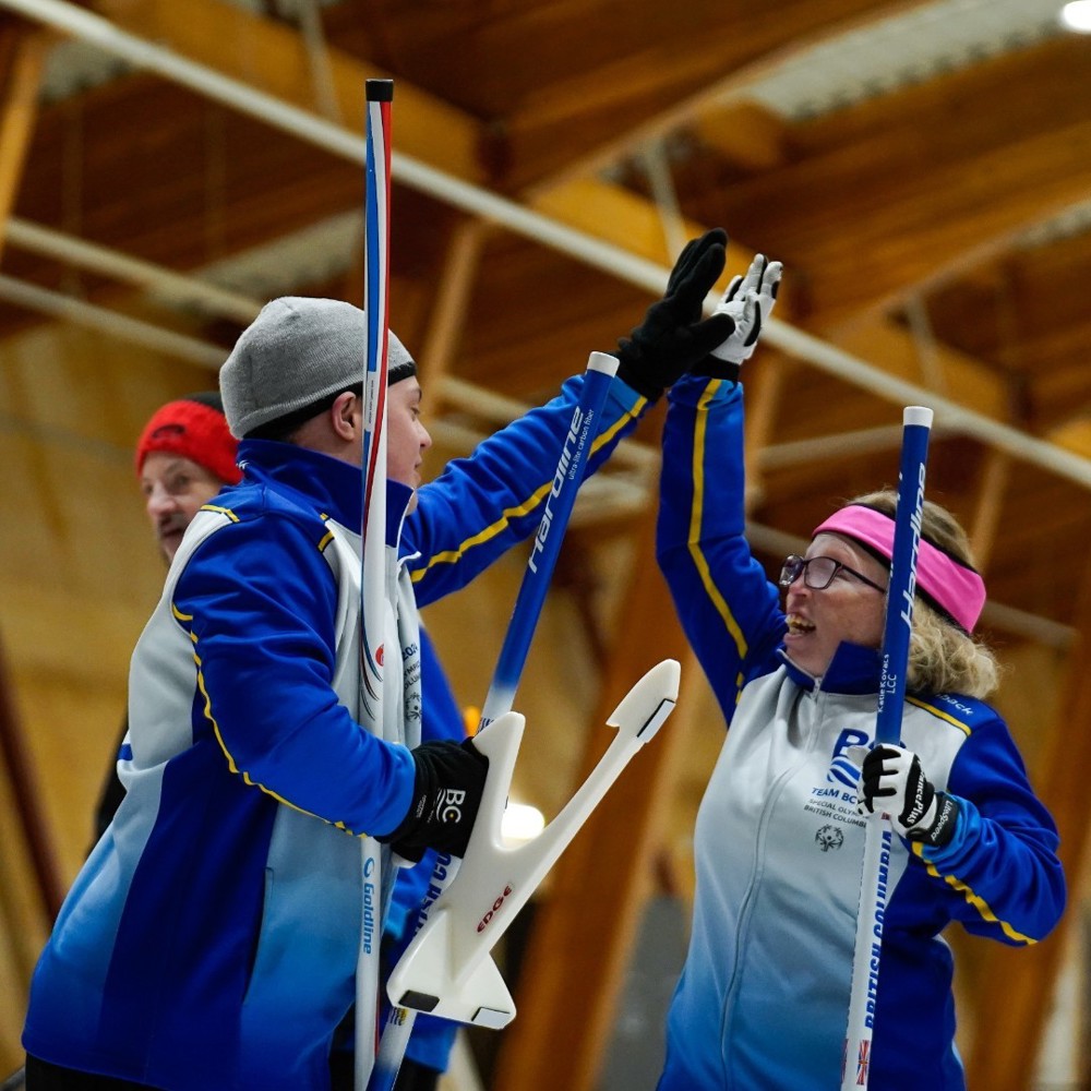 Two Special Olympics BC curling athletes celebrate with a jubilant high-five.