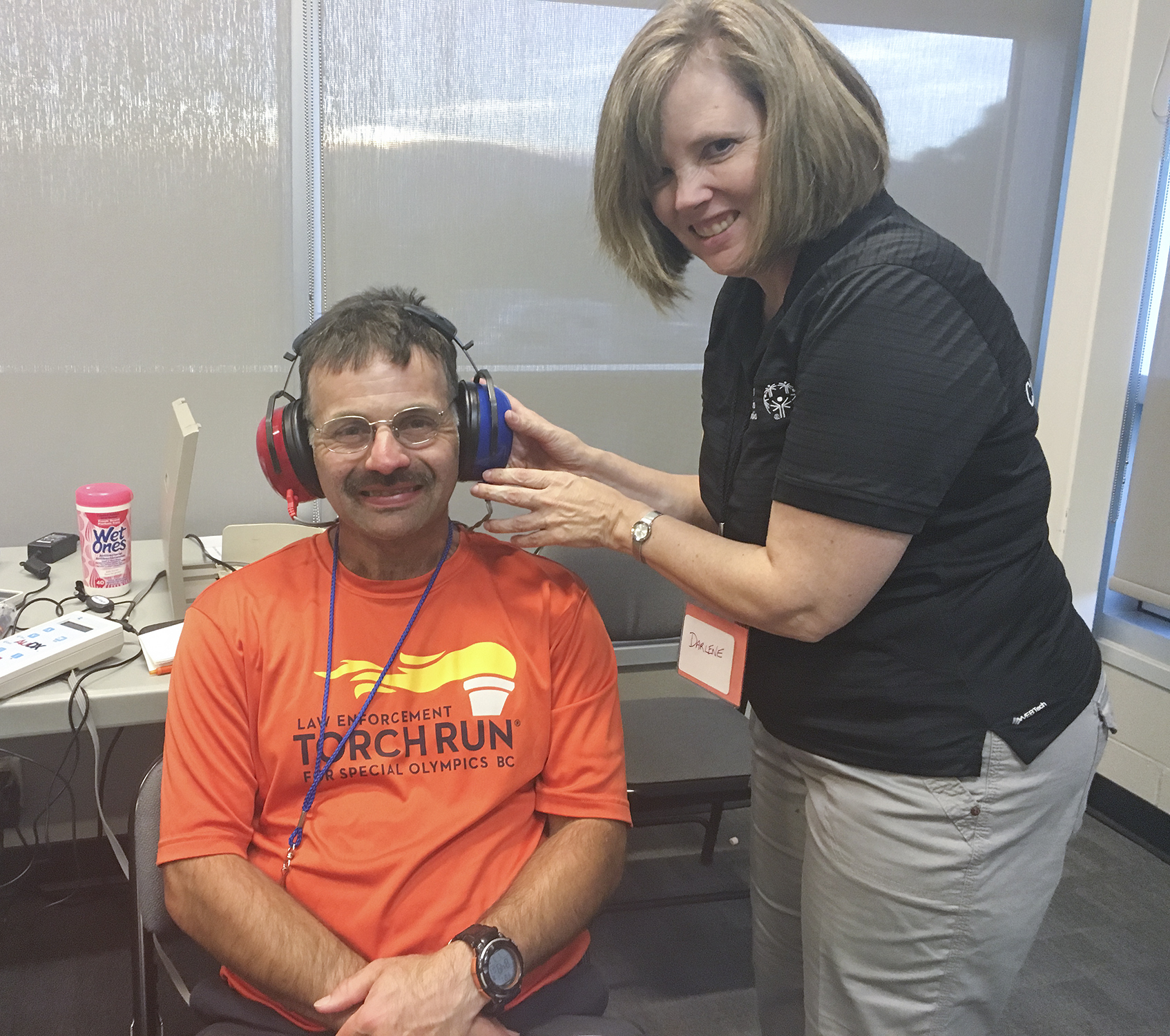 A man with large headphones on smiles for a photo next to a woman at a Healthy Hearing event.