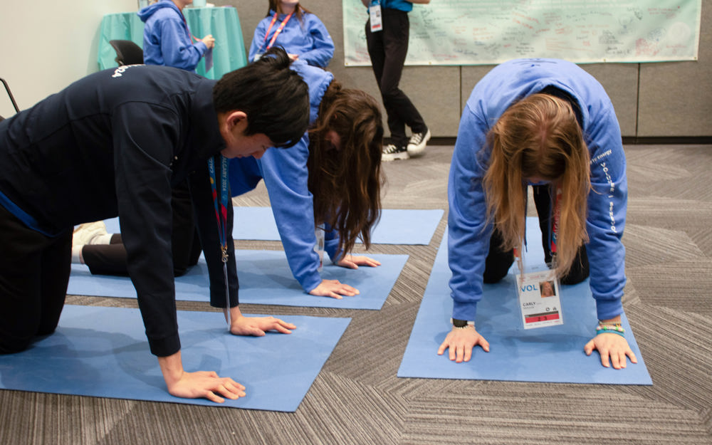 A volunteer and two athletes do yoga on blue mats.