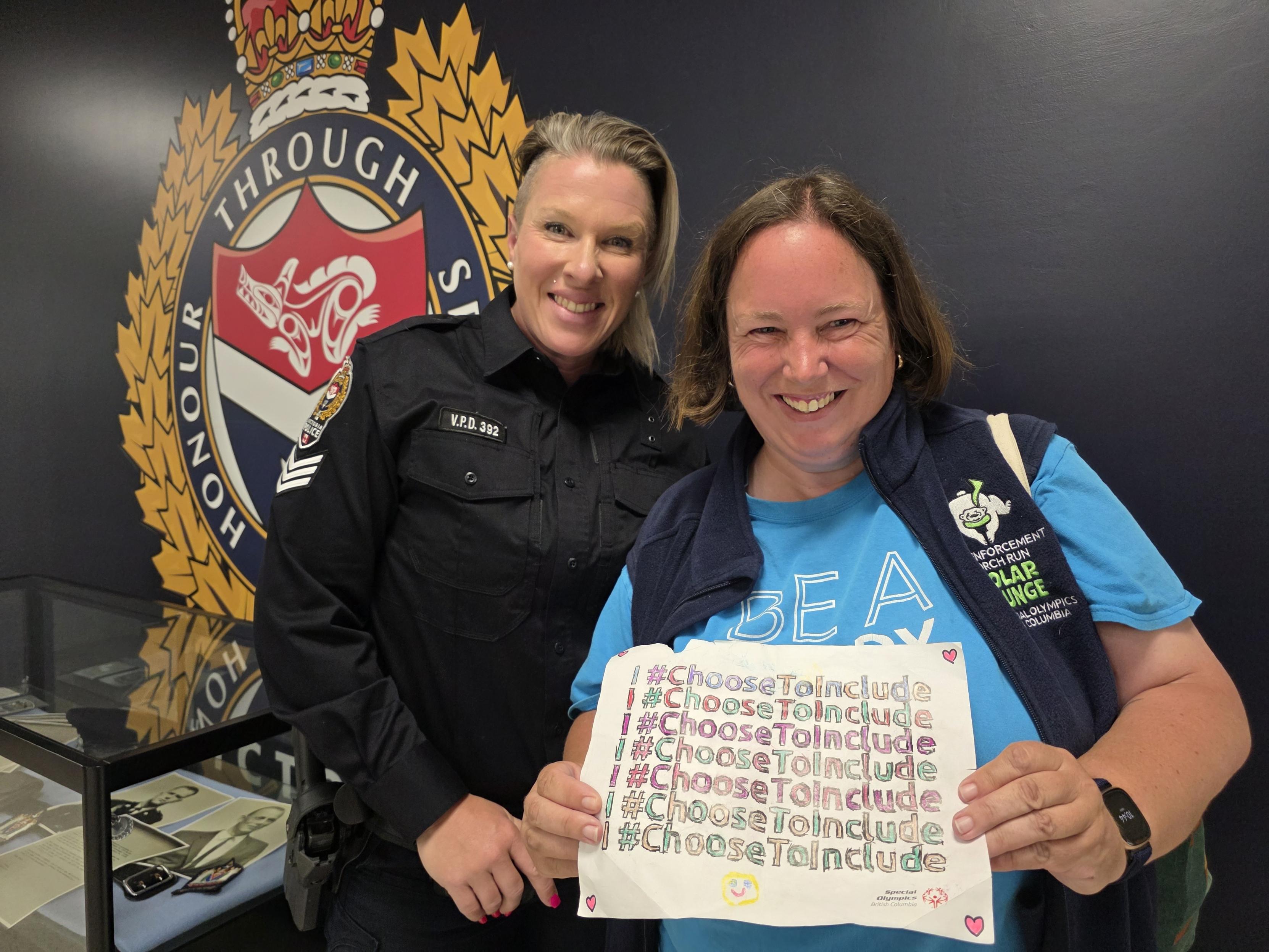 Law enforcement member and athlete smiling holding a picture saying "I Choose To Include"